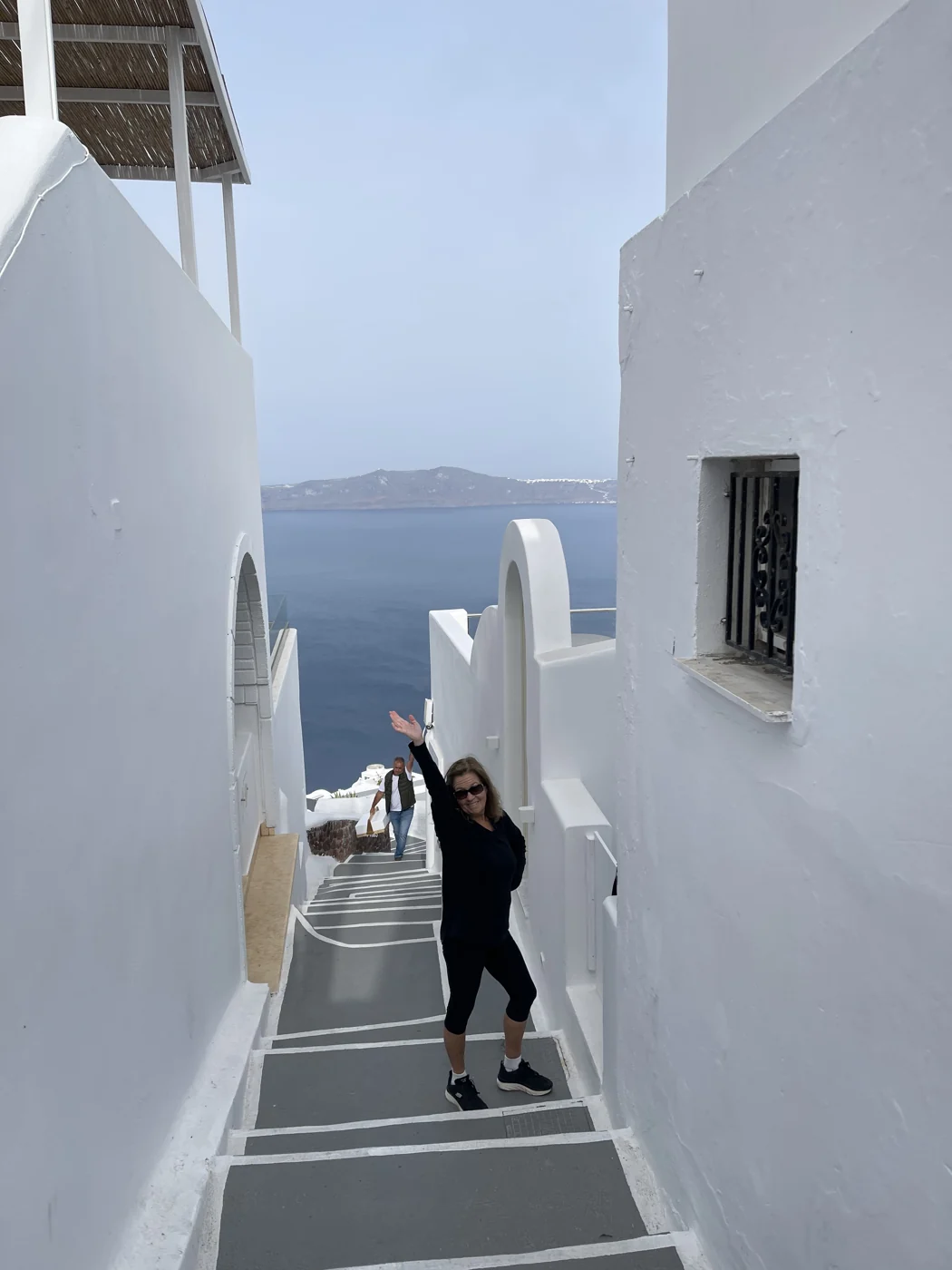 Connie waving on a whitewashed stairway above the sea in Greece